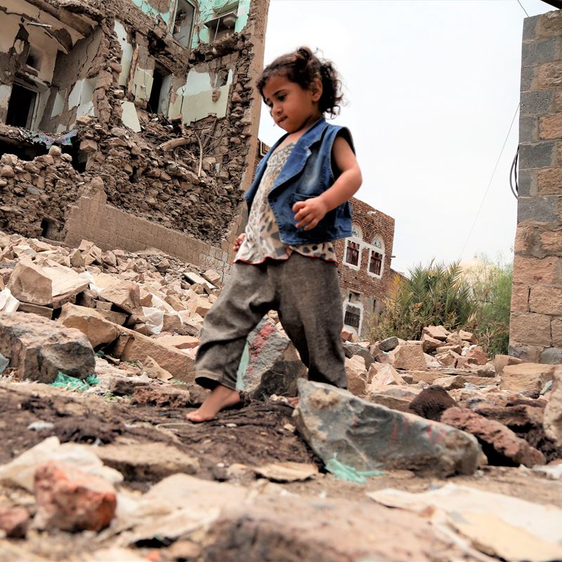 Barn går gennem ruinerne af bombede bygninger i Yemen. 